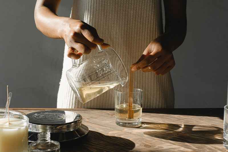 Pouring melted wax into a glass container to make a candle