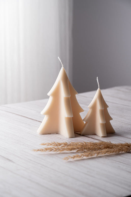 Two beige tree-shaped candles on a white surface with a blurred background